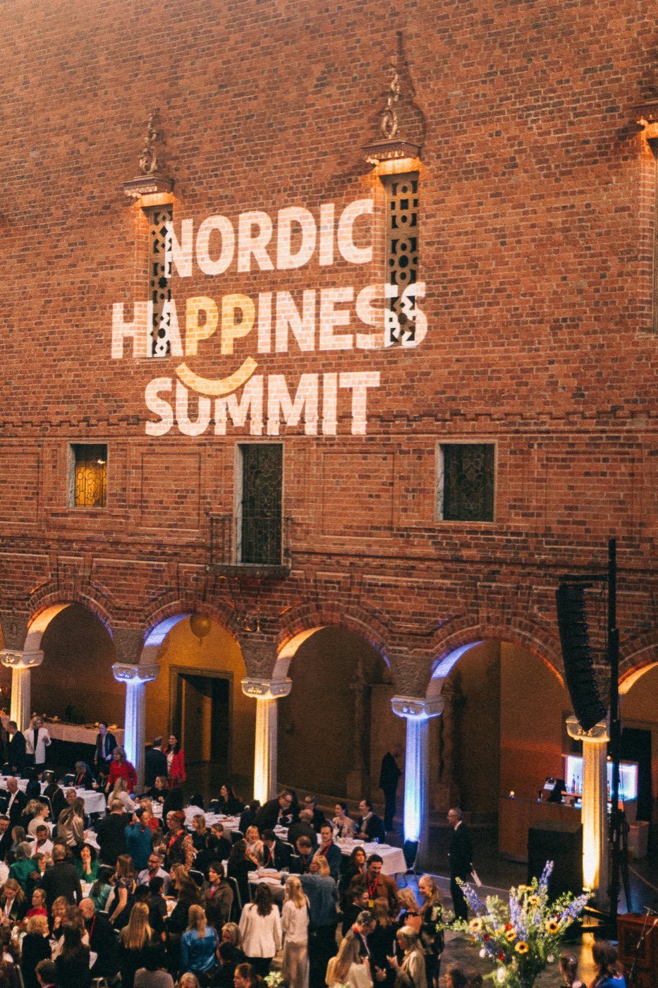 The Nordic Happiness Summit logo projected on the brick wall of the Blue Hall above the arched colonnade and guests below
